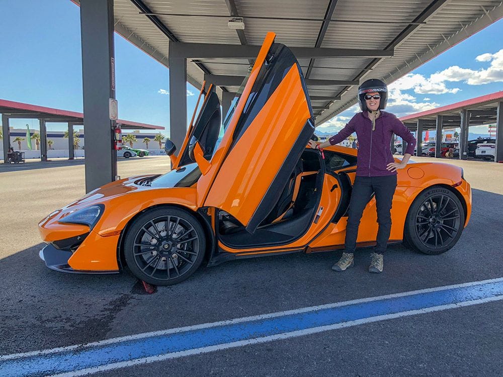 Lydia standing next to an orange McLaren 570s sports car