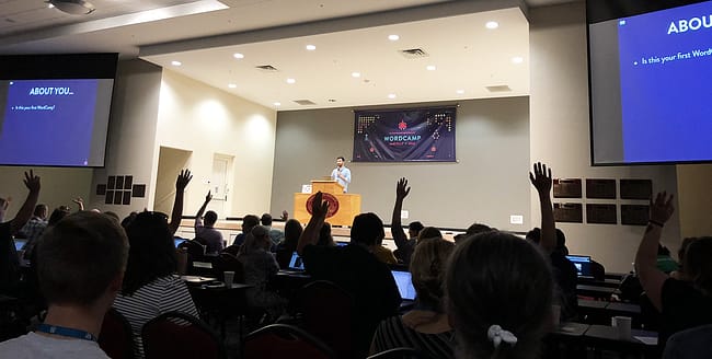 People raise their hands during the opening announcements of WordCamp Asheville 2018
